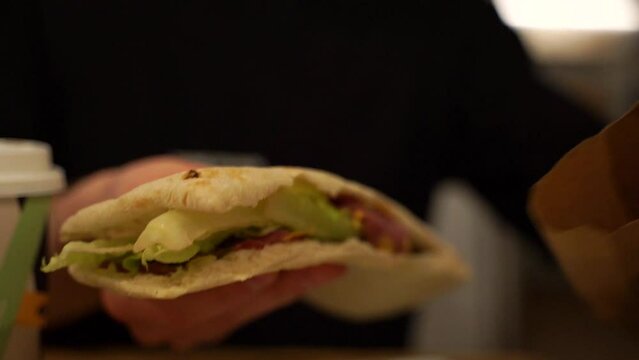 A man sits at a table in a restaurant and eats a sandwich