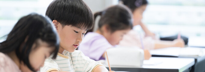 小学校の教室で勉強する小学生の子供たち　テストや試験を受けるバナー