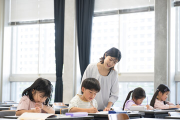 学校の教室で勉強する複数(多人数)の子供たちと指導する先生の広角