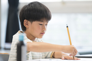 明るい小学校の教室で習字を教わる小学生の男の子　クローズアップ