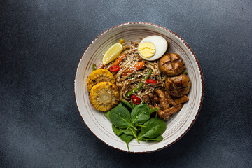 Asian cuisine. Noodles with egg and corn in a plate. On a dark background