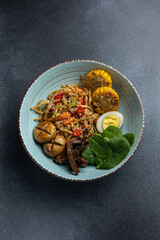 Asian cuisine. Noodles with egg and corn in a plate. On a dark background