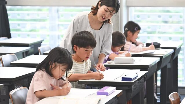学校の教室で勉強する複数(多人数)の子供たちと指導する先生の動画