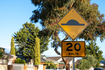 A traffic warning sign indicates the presence of a speed hump on the road with a 20km/h speed...