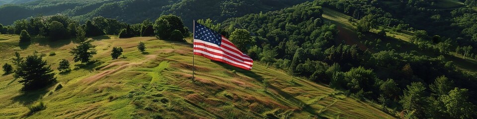 An aerial view of a large United States flag displayed on a hillside, surrounded by lush green trees and open sky.