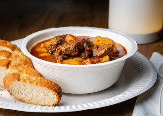 Guiso húngaro (goulash) servido en un bol blanco, acompañado de pan fresco en un plato blanco. Plato robusto con carne, papas y zanahorias, ideal para comida casera reconfortante.