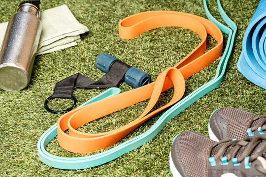 Equipo de ejercicio sobre c&eacute;sped: botella de agua, toalla, bandas el&aacute;sticas, correas de entrenamiento y zapatos deportivos. Ideal para actividades al aire libre y rutinas de fitness.