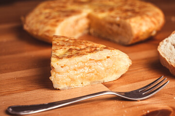 Pedazo de tortilla de patatas Española en primer plano sobre un fondo de madera y en segundo plano el resto de la tortilla.
