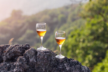 Two glasses of champagne on the top rock mountain at sunset background
