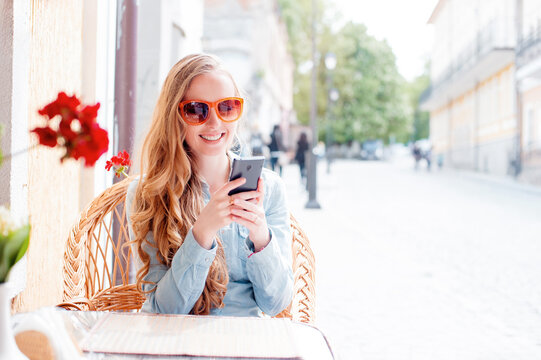 Cafe with wifi. Young attractive smiling woman using smart phone while sitting at sidewalk restaurant.