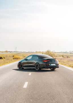 Photo of a black Mercedes-Benz AMG CLA 45 S 4MATIC+. They show details of the car from the outside. Rims, emblems, headlights, lamps in a sporty style. The model stands in the middle of highway.