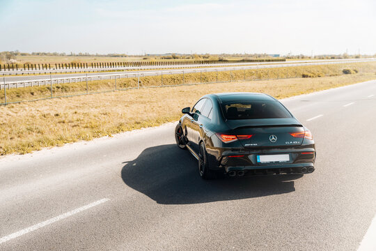 Photo of a black Mercedes-Benz AMG CLA 45 S 4MATIC+. They show details of the car from the outside. Rims, emblems, headlights, lamps in a sporty style. The model stands in the middle of highway.
