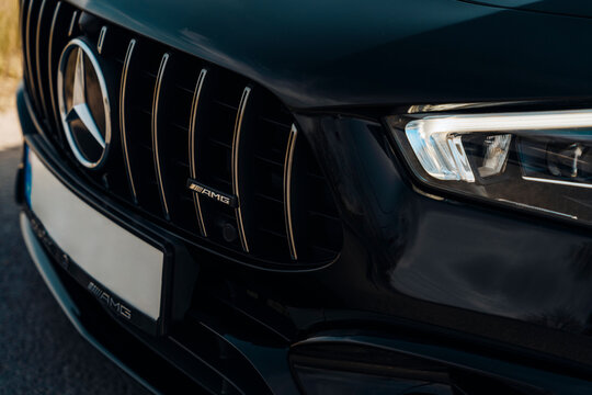 Photo of a black Mercedes-Benz AMG CLA 45 S 4MATIC+. They show details of the car from the outside. Rims, emblems, headlights, lamps in a sporty style. The model stands in the middle of highway.