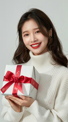 Fototapeta premium happy woman in white sweater is holding a white box with a red ribbon