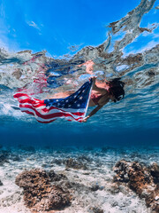 Woman snorkeling underwater in blue sea with US flag. Independence day concept.