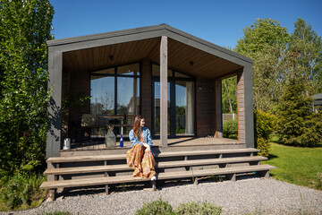 A woman sits on the terrace of a barnhouse. Wooden secluded house in Scandinavian and Finnish...