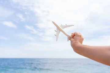 Hand holding a miniature airplane and making it fly with a beautiful beach in the background in the...