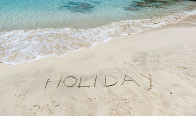 The word holiday written in the sand on the beach in front of the sea