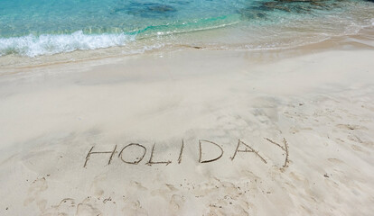 The word holiday written in the sand on the beach in front of the sea