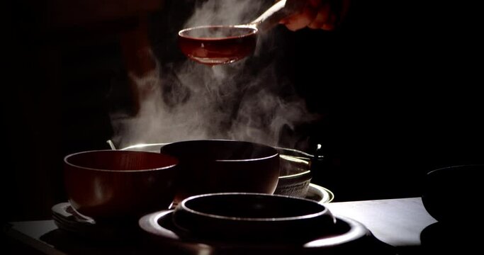Slow motion scene of a retro-style restaurant as a cook ladles steaming hot food with a wooden ladle into a wooden bowl.