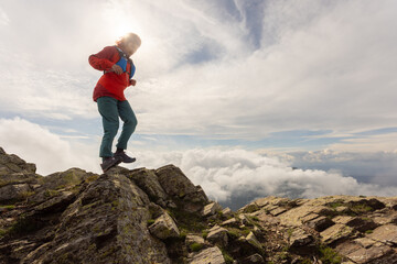 Obraz premium A woman is standing on a mountain top, wearing a red jacket and blue pants