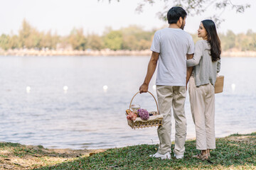 Asian couple walking in garden with picnic basket. in love couple is enjoying picnic time in park...