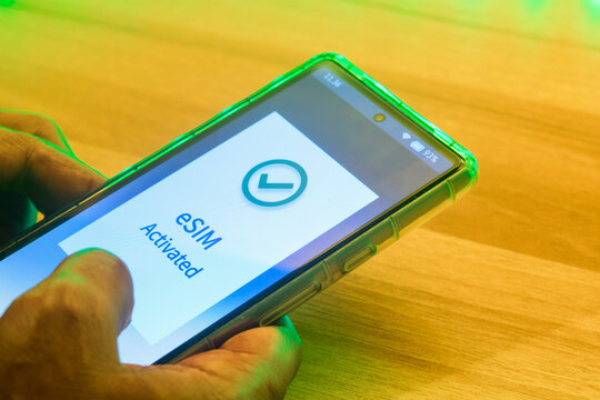 Mobile phone in hand displaying the message eSIM activated. Digital SIM to allow cellular connection, night time, close up image.