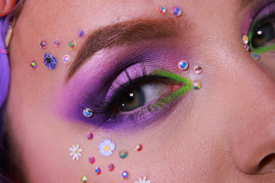 Stunning spring purple and neone green eye makeup with doll eyeslahes, flowers and perals. Girly makeup for spring and summer festivals. Close up on face.