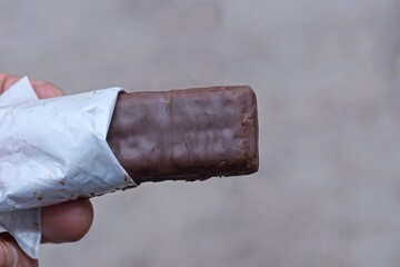 hand holding one brown chocolate bar outdoors on gray background