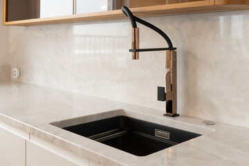 Close-up of a sleek, modern kitchen faucet with a marble countertop and sink. The minimalist design...