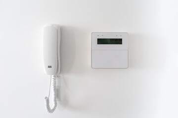 A white intercom system paired with a digital display, mounted on a pristine white wall. This...