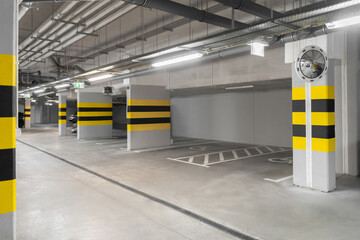 A wide, well-lit underground parking garage featuring clear markings and yellow-black striped...