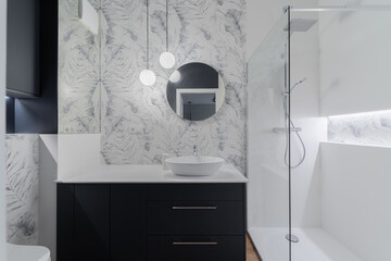 A sleek modern bathroom featuring a stylish vanity with a round mirror, glass shower enclosure, and...