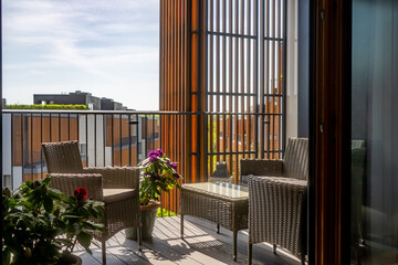 A stylish modern balcony featuring wicker furniture and vibrant potted plants. The urban view and...