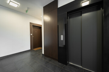 A modern apartment building elevator lobby featuring dark wood panels and sleek tile flooring. The...