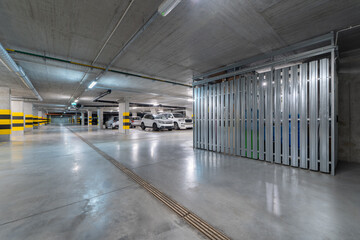 A spacious underground parking garage featuring bright lighting, clearly marked parking spaces, and secure storage areas.