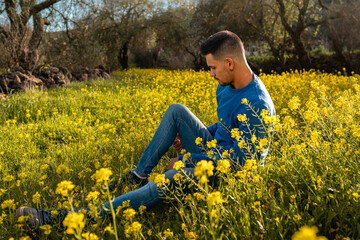 Fototapeta premium young man in a field of yellow wildflowers at sunset