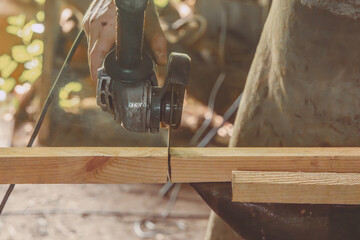 Hand of a craftsman with a circular saw sawing wooden blocks in an outdoor workshop. Close-up