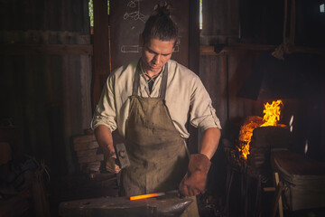 Blacksmith forges a red-hot metal piece on an anvil in a forge. Traditional crafts