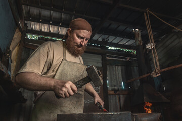 Blacksmith forges a red-hot metal piece on an anvil in a rural forge. Traditional crafts