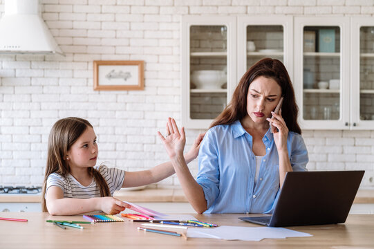 Busy freelance woman working from home, talking via smartphone, watching little kid