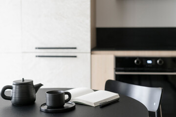 Coffee cup near diary journal in kitchen with classic chair and black table