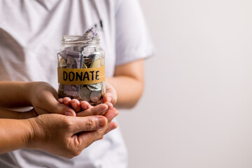 Woman holding coins and cash in jar with words Give or Donate elegantly lettered on its front, embodying spirit of giving. words, lettering, donate, jar, money, giving, woman, give, coin.