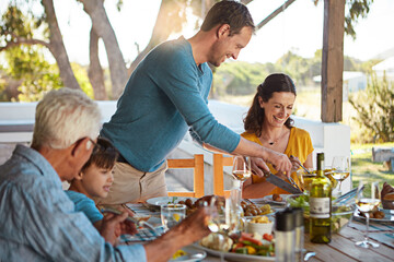 Happy family, eating and lunch with laughing outdoor on patio with funny people, bonding or healthy food. Parents, grandparents and kids at dining table in backyard of home with love or talking