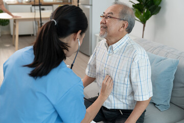 Asian young woman caregiver doctor using stethoscope to checking heartbeat elderly man patient in room during home visit