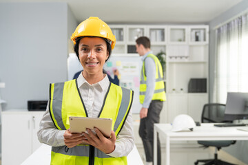 Portrait of confident female engineer standing and holding tablet at construction office. Woman foreman wearing vest and hardhat safety ready to team