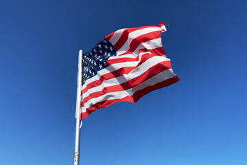 Fototapeta premium United State of America flag flutters in the wind on blue sky background, Travel and tourism in USA concept, election in USA 2024