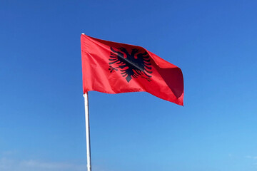 Red Albanian flag with double-headed black eagle flutters in the wind on blue sky background, Travel and tourism in Balkan concept