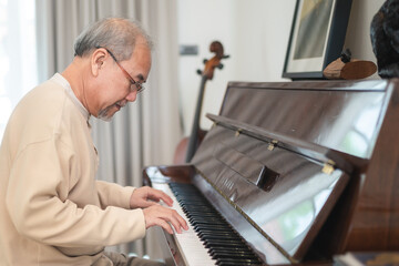 Happy relaxation Asian senior retirement man with eyeglasses learn to play piano at home, elderly old man playing music on piano in living room, lifestyle life after retirement, Close up hands © chokniti