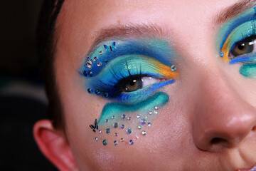 Fototapeta premium Vibrant ocean summer festival shimmery eye makeup with bold eyeslahes. Shiny glitter effect in blue and yellow colors with crystals